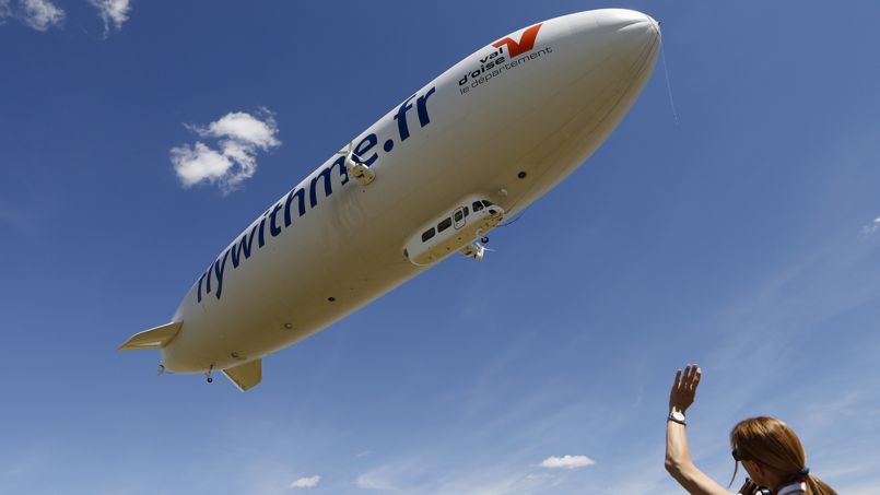 A ground crew member waves as a semi-rigid and helium-filled Zeppelin NT departs from a field at an airport outside Cergy-Pointoise